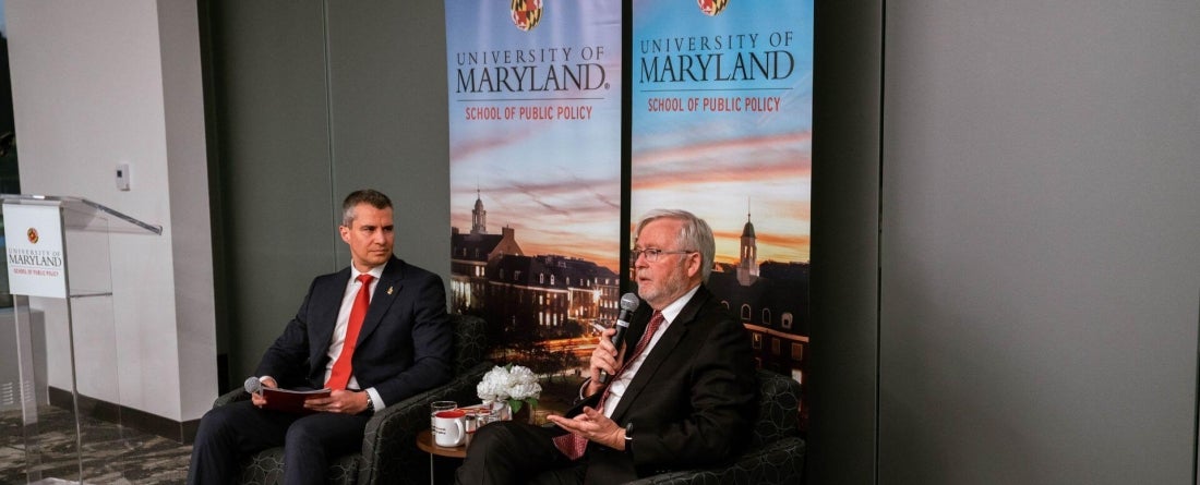 image of Dean Gustavo Flores-Macias and Ambassador Kevin Rudd sitting in chairs talking in front of 2 UMD banners with a table in between them
