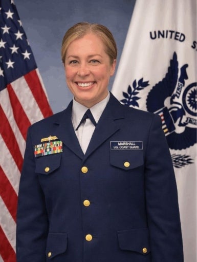 headshot of Elizabeth Jordan Marshall, a white woman with blond hair dressed in a Coast Guard uniform and standing in front of a USA flag and a Coast Guard flag
